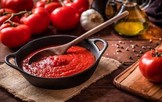 High angle view of a rustic cooking pan full of homemade tomato sauce surrounded by various tomatoes, garlic, pepper and olive oil for preparing the source. Predominant colors are brown and red, Studio shot taken with Canon EOS 6D Mark II and Canon EF 24-105 mm f/4L