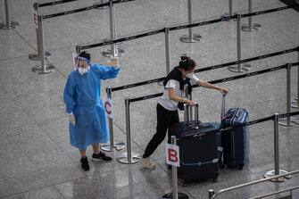 epa10066299 A health worker in protective gown directs a woman to transportation to her quarantine hotel in the arrival hall at Hong Kong International Airport in Hong Kong, China, 12 July 2022. Under a government proposal for a health code system, people arriving in Hong Kong confirmed to have been infected by the Covid-19 coronavirus will be issued a red code, while inbound travellers who have completed their mandatory 7-nights hotel quarantine but are still under monitoring will be given a yellow code.  EPA/JEROME FAVRE