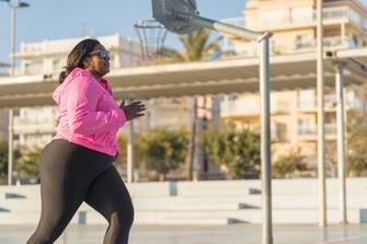 African American female athlete in sportswear and sneakers jogging on city street