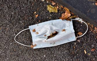 Discarded disposable face mask ending as waste on pavement in city