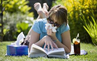 A woman suffering from hay fever while sunbathing in her garden.