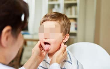 Pediatrician feels the tonsils in a child with a sore throat and shows his tongue