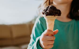 A child grips a small wafer cone with a serving of chocolate ice-cream. Space for copy.