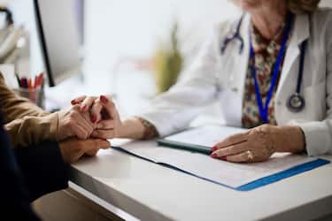 Shot of an unrecognizable doctor holding hands with her patients during a consultation