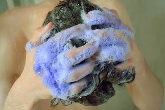 Young man washing his hair with a purple shampoo
