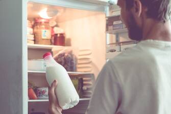 young bearded man opens the bottle of milk standing near the fridge at home