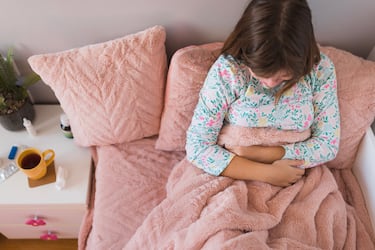 Girl in pajamas resting in bed when having a strong stomachache