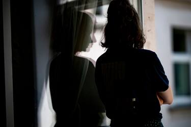 PRODUCTION - 13 July 2021, Berlin: ILLUSTRATION - A woman stands at a window in her apartment with her arms crossed. (posed scene) Photo: Fabian Sommer/dpa (Photo by Fabian Sommer/picture alliance via Getty Images)