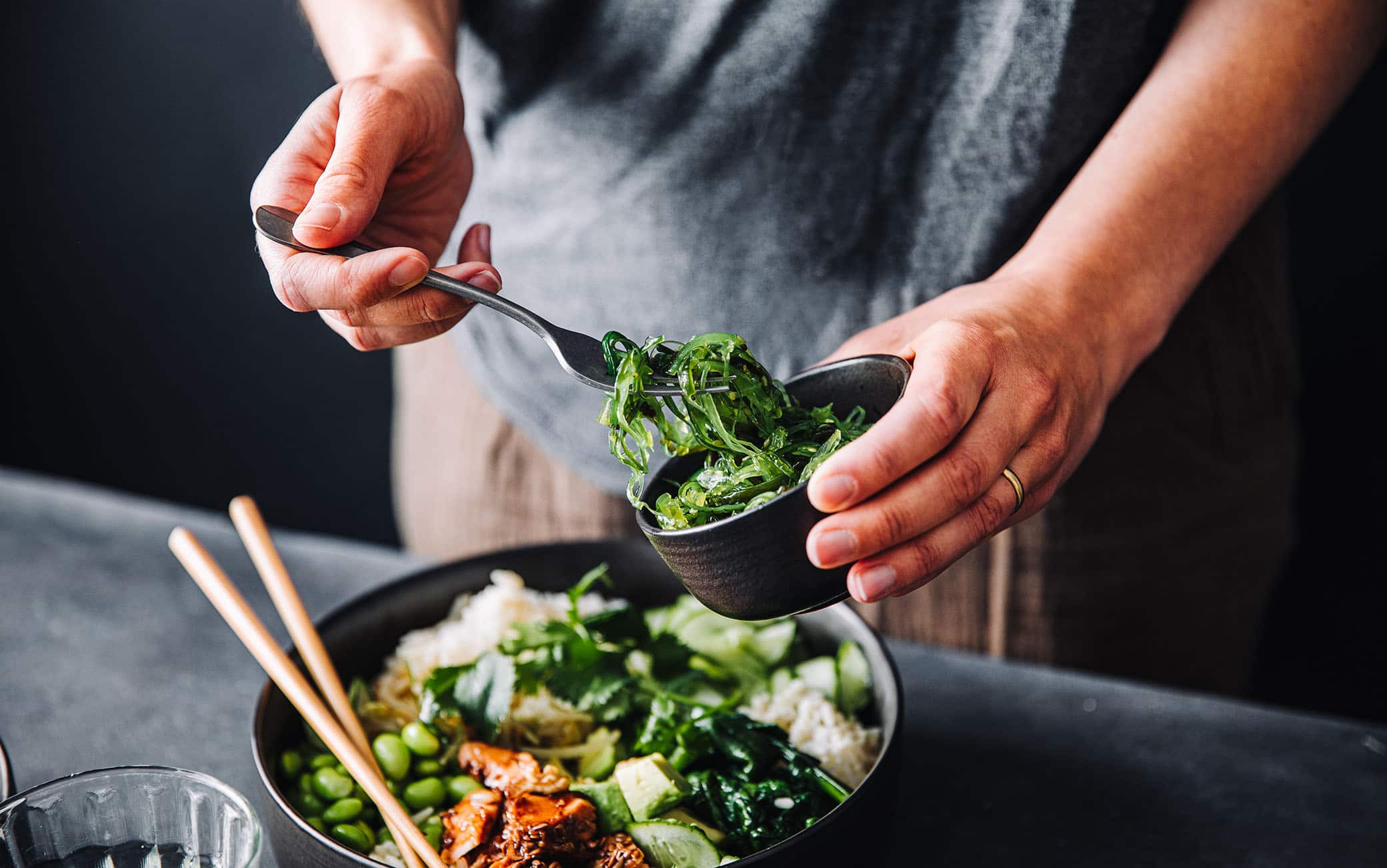 Close-up of woman eating omega 3 rich salad. Female having healthy salad consist of chopped salmon, spinach, brussels sprouts, avocado, soybeans, wakame and chia seeds in a bowl.