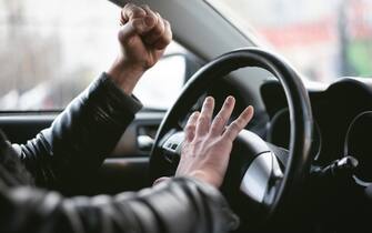 Angry driver is honking and is yelling by sitting of a steering wheel. Road aggression concept. Traffic jam.