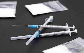 Drug injection syringe and cooked heroin in a bag on black background