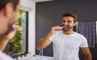 Nice and fresh for the day. a handsome man looking in the mirror and brushing his teeth in the bathroom at home.