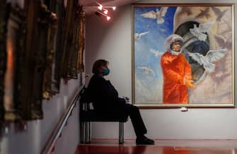 epa09125137 A museum worker sits next to a painting by  Soviet cosmonaut Vladimir Dzhanibekov, titled 'Gagarin before the start', at the Museum of Cosmonautics in Moscow, Russia, 09 April 2021. The museum is dedicated to space exploration, with exhibits, items, and models related to the Soviet and Russian space eras on display. Russia marks the 60th anniversary of the first human spaceflight on 12 April 2021.  EPA/SERGEI ILNITSKY