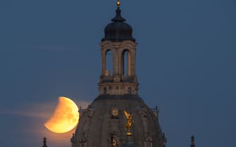 16 May 2022, Saxony, Dresden: The moon sets in the morning during a partial lunar eclipse behind the Frauenkirche and the dome of the Kunstakedmie with the angel "Fama". Onlookers can watch a total lunar eclipse this morning, but not everywhere. In some places the moon will already disappear behind the horizon in the southwest before it completely dives into the earth's shadow. So observers could partly only watch a partial lunar eclipse. Photo: Robert Michael/dpa (Photo by Robert Michael/picture alliance via Getty Images)