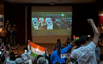 People wave India's national flag as India's Prime Minister Narendra Modi (C screen) congratulates the Indian Space Research Organisation (ISRO) for the successful lunar landing of Chandrayaan-3 spacecraft on the south pole of the Moon during a live stream of the event at the Nehru Science Centre in Mumbai on August 23, 2023. India on August 23, became the first nation to land a craft near the Moon's south pole, a historic triumph for the world's most populous nation and its ambitious, cut-price space programme. (Photo by Punit PARANJPE / AFP) (Photo by PUNIT PARANJPE/AFP via Getty Images)