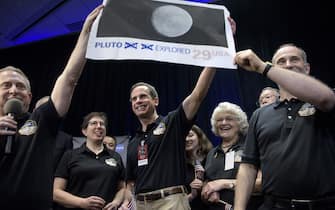 480657646 Dr. Allan Stern (L), principal investigator for the New Horizons mission to Pluto, and others hold up their suggestion for a modified US Post Office stamp of Pluto at the Johns Hopkins University Applied Physics Laboratory to celebrate the closest fly-by of the New Horizons probe July 14, 2015 in Laurel, Maryland. The unmanned NASA spacecraft whizzed by Pluto on JUly 14, making its closest approach in the climax of a decade-long journey to explore the dwarf planet for the first time, the US space agency said. Moving faster than any spacecraft ever built -- at a speed of about 30,800 miles per hour (49,570 kph) -- the flyby happened at 7:49 am (1149 GMT), with the probe running on auto-pilot. It was to pass by Pluto at a distance of 7,767 miles (12,500 kilometers). Looking on 2nd-Right is Annette Tombaugh, daughter of the man who discovered Pluto, Clyde Tombaugh. AFP PHOTO/BRENDAN SMIALOWSKI (Photo credit should read BRENDAN SMIALOWSKI/AFP via Getty Images)