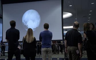 480658768 People look at an early image of Pluto taken by the New Horizons probe as the craft makes its closest fly-by of the dwarf planet at the Johns Hopkins University Applied Physics Laboratory July 14, 2015 in Laurel, Maryland. The unmanned NASA spacecraft whizzed by Pluto on July 14, making its closest approach in the climax of a decade-long journey to explore the dwarf planet for the first time, the US space agency said. Moving faster than any spacecraft ever built -- at a speed of about 30,800 miles per hour (49,570 kph) -- the flyby happened at 7:49 am (1149 GMT), with the probe running on auto-pilot. It was to pass by Pluto at a distance of 7,767 miles (12,500 kilometers). AFP PHOTO/BRENDAN SMIALOWSKI (Photo credit should read BRENDAN SMIALOWSKI/AFP via Getty Images)