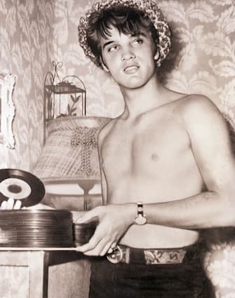Elvis Presley, hatted and shirtless, holds a stack of 45's of "That's All Right, Mama," his first commercial recording.