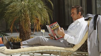 Scottish actor Sean Connery relaxes on the set of the James Bond film 'Diamonds Are Forever', USA, May 1971. He is reading the 12th April 1971 edition of 'TIME' magazine, with Lieutenant William Calley Jr. on the cover. (Photo by Anwar Hussein/Getty Images)