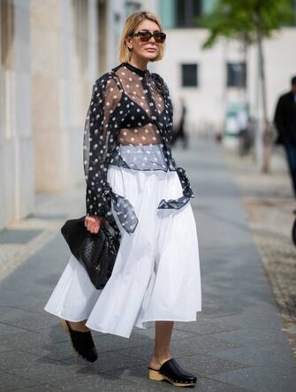BERLIN, GERMANY - MAY 08: Victoria Nasir is seen wearing white pleated poplin a-line skirt COS, transparent blouse with polka dots Petar Petrov, clogs Zara, black the pouch Bottega Venta, sunglasses Marni on May 08, 2019 in Berlin, Germany. (Photo by Christian Vierig/Getty Images)
