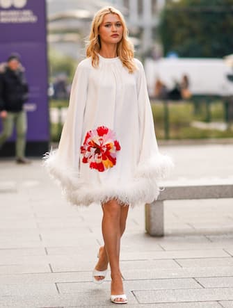 1207680389 MILAN, ITALY - FEBRUARY 20: Chloe Lecareux wears a white dress with embroidered red/pink flower and fluffy parts, white shoes, outside Vivetta, during Milan Fashion Week Fall/Winter 2020-2021 on February 20, 2020 in Milan, Italy. (Photo by Edward Berthelot/Getty Images)