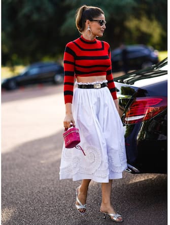 PARIS, FRANCE - JUNE 29: Laetitia Casta wears large earrings, sunglasses, a red and black cropped bare belly top, a belt, a white skirt with embroidery, a pink bag, silver shoes, outside Miu Miu Club 2020,  on June 29, 2019 in Paris, France. (Photo by Edward Berthelot/Getty Images)