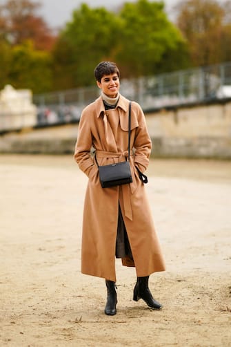 1283948827 PARIS, FRANCE - SEPTEMBER 29: A model wears a brown trench coat, a wool turtleneck pullover, a black leather bag, black leather boots, outside Dior, during Paris Fashion Week - Womenswear Spring Summer 2021 on September 29, 2020 in Paris, France. (Photo by Edward Berthelot/Getty Images)