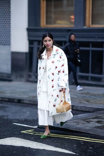 1131234221 LONDON, ENGLAND - FEBRUARY 18: Bettina Looney wears earrings, a white floral print coat, a white frilly dress, a rectangular box bag, green suede mules, during London Fashion Week February 2019 on February 18, 2019 in London, England. (Photo by Edward Berthelot/Getty Images)