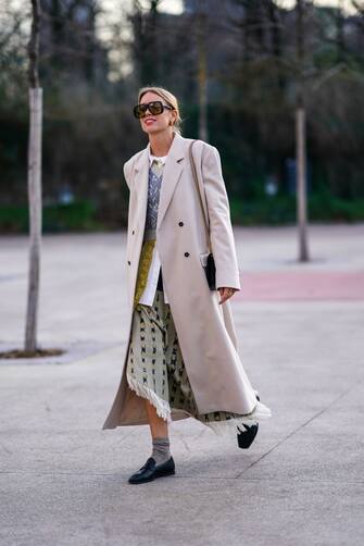 PARIS, FRANCE - JANUARY 18: A guest wears sunglasses, a gray long coat, a white long shirt, a wool pullover, a fringed skirt, gray socks, black leather shoes, outside Jacquemus, during Paris Fashion Week - Menswear F/W Fall/Winter 2020-2021 on January 18, 2020 in Paris, France. (Photo by Edward Berthelot/Getty Images)