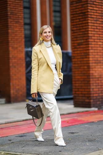 1282283190 PARIS, FRANCE - OCTOBER 03: Xenia Adonts wears golden earrings, a white turtleneck pullover, a pale yellow oversized blazer jacket, a brown Hermes bag, a golden chain necklace, white flared silky lustrous pants, white leather pointy shoes, outside Hermes, during Paris Fashion Week - Womenswear Spring Summer 2021 on October 03, 2020 in Paris, France. (Photo by Edward Berthelot/Getty Images)