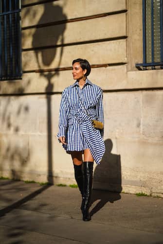 1303917905 PARIS, FRANCE - FEBRUARY 23: Adriana Seminario wears earrings, a blue and white checked pattern printed dress from Marques Almeida, a golden metallic Saint-Laurent YSL bag, thigh high leather black pointy boots from Mi/Mai, on February 23, 2021 in Paris, France. (Photo by Edward Berthelot/Getty Images)