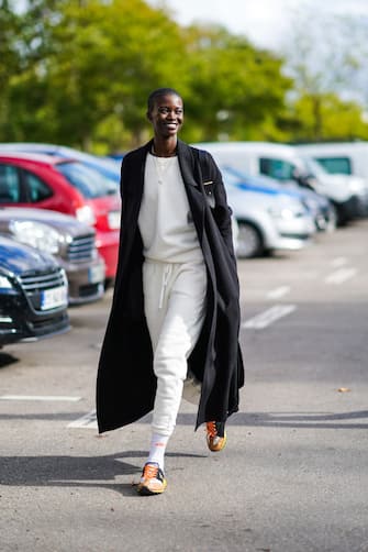 PARIS, FRANCE - OCTOBER 03: A model wears a black long wool coat, a white pullover, a necklace, sportswear cropped white jogger pants, Ellesse socks, orange Y-3 sneakers shoes, outside Hermes, during Paris Fashion Week - Womenswear Spring Summer 2021 on October 03, 2020 in Paris, France. (Photo by Edward Berthelot/Getty Images)