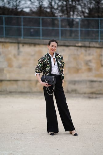 PARIS, FRANCE - MARCH 10: Alba Garavito Torre wears a white shirt from Zara, a green and khaki military print bomber jacket from Mr&Mrs Italy, a black leather quilted Chanel bag, black flare suit pants from Munthe, Chanel slingback shoes, golden bracelets, golden earrings, on March 10, 2021 in Paris, France. (Photo by Edward Berthelot/Getty Images)