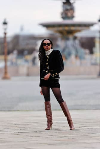 PARIS, FRANCE - MARCH 05: Emilie Joseph @in_fashionwetrust wears sunglasses, a black military velvet jacket with golden buttons from Saint Laurent YSL, a turtleneck white ruffle top with mesh lace and floral embroidery from &OtherStories, black shorts, black tights, brown leather crocodile pattern pointy knee-high high heels boots from Paris Texas, on March 05, 2021 in Paris, France. (Photo by Edward Berthelot/Getty Images)