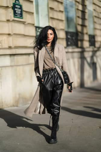 PARIS, FRANCE - FEBRUARY 23: Damy Aghlam aka "Gamine de Paris" wears a beige long wool coat, a brown t-shirt, black leather pants, a black woven leather Bottega Veneta bag with a metallic chain, black leather knee high combat / military boots with shoelace, on February 23, 2021 in Paris, France. (Photo by Edward Berthelot/Getty Images)