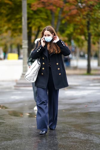 PARIS, FRANCE - OCTOBER 06: A guest wears a face mask, a black oversized large military jacket with golden buttons, navy blue flared pants, black leather pointy shoes, a white large bag, outside Chanel, during Paris Fashion Week - Womenswear Spring Summer 2021, on October 06, 2020 in Paris, France. (Photo by Edward Berthelot/Getty Images)