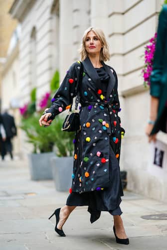 LONDON, ENGLAND - SEPTEMBER 16: A guest wears a black lustrous kimono long jacket with colored embroidered pompoms, black high heel pumps shoes, a bag, during London Fashion Week September 2019 on September 16, 2019 in London, England. (Photo by Edward Berthelot/Getty Images)