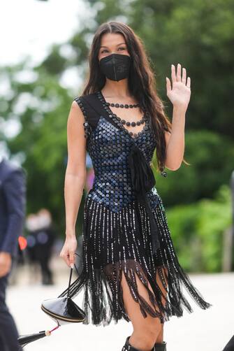PARIS, FRANCE - JULY 05: Bella Hadid wears a black pearls necklace from Louis Vuitton, a black sequins / glitter shiny sleeveless short dress with knot on the chest and tulle fringes with sequins on the skirt, a black shiny leather embossed with LV monogram handbag from Louis Vuitton, black shiny grained leather knees boots from Louis Vuitton, outside Louis Vuitton Parfum hosts dinner at Fondation Louis Vuitton, during Paris Fashion Week - Haute Couture Fall/Winter 2021/2022, on July 05, 2021 in Paris, France. (Photo by Edward Berthelot/Getty Images)