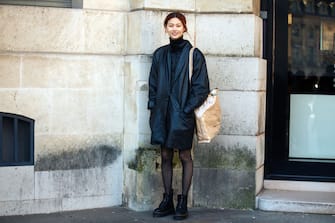 PARIS, FRANCE - FEBRUARY 28: Korean model Hoyeon Jung wears an all-black outfit including an oversized leather jacket, a down jacket, a turtleneck, stockings, combat boots, and a tan Comme des Garcons  Shirt paper/plastic tote bag on February 28, 2018 in Paris, France. (Photo by Melodie Jeng/Getty Images)