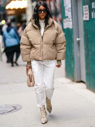 NEW YORK, NEW YORK - FEBRUARY 08: A guest wears sunglasses, a white turtleneck pullover, a pale pastel brown oversized puffer coat, white pants, snake print pointy leather boots, a bag, outside Hellessy, during New York Fashion Week Fall-Winter 2020, on February 08, 2020 in New York City. (Photo by Edward Berthelot/Getty Images)