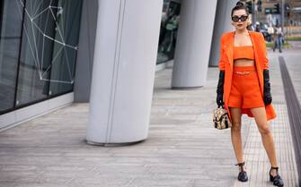 MILAN, ITALY - FEBRUARY 24: Karina Nigay poses ahead of the Max Mara fashion show wearing an orange coat and shorts and black long glows during the Milan Fashion Week Fall/Winter 2022/2023 on February 24, 2022 in Milan, Italy. (Photo by Claudio Lavenia/Getty Images)