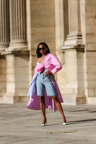 PARIS, FRANCE - JUNE 12: Emilie Joseph @in_fashionwetrust wears black sunglasses, a striped two toned pale blue and pink maxidress by JournÃ©e worn as a long shirt, a baby pink boyfriend shirt worn off shoulder and tied in the front, blue denim dad ripped shorts/bermudas, crystal ring by Swarovski Collection I by Giovanna Engelbert and earrings, pale green pointy pumps by Jimmy Choo, on June 12, 2021 in Paris, France. (Photo by Edward Berthelot/Getty Images)