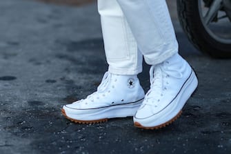 MILAN, ITALY - JANUARY 16: A guest wears white denim jeans pants, white Run Away ankle sneakers from Converse, outside the Prada  fashion show during the Milan Men's Fashion Week - Fall/Winter 2022/2023 on January 16, 2022 in Milan, Italy. (Photo by Edward Berthelot/Getty Images)