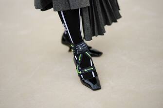 PARIS, FRANCE - SEPTEMBER 27: A guest wears a gray pleated long skirt, black with white striped print pattern socks from Dior, black shiny varnished leather with neon green seams ankle ballerinas from Dior , outside Dior, during Paris Fashion Week - Womenswear Spring/Summer 2023, on September 27, 2022 in Paris, France. (Photo by Edward Berthelot/Getty Images)