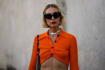 MILAN, ITALY - SEPTEMBER 22: A guest wears silver hair clips, black sunglasses, silver large chain necklaces, an orange ribbed buttoned / long sleeves cropped pullover, a black shiny leather with embroidered rhinestones Cleo shoulder bag from Prada, outside Prada, during the Milan Fashion Week - Womenswear Spring/Summer 2023 on September 22, 2022 in Milan, Italy. (Photo by Edward Berthelot/Getty Images)