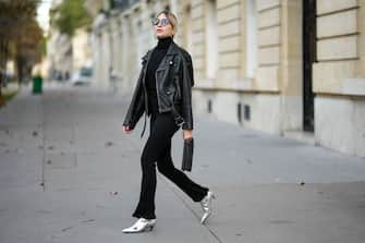 PARIS, FRANCE - OCTOBER 26: Emy Venturini wears black cat eyes sunglasses, gold earrings, a black ribbed wool turtleneck pullover from Intimissimi, a black shiny leather biker jacket from Saint Laurent Paris, black flared pants from Cos, a black shiny leather clutch from Saint Laurent Paris, silver shiny varnished leather pointed heels shoes from Balenciaga, during a street style fashion photo session, on October 26, 2022 in Paris, France. (Photo by Edward Berthelot/Getty Images)