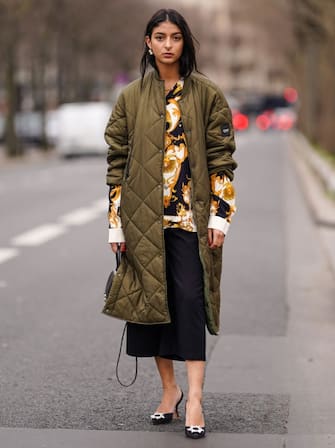 PARIS, FRANCE - MARCH 22: Melanie Darmon wears a green khaki long quilted padded puff winter coat from Aigle, a black yellow and white floral print shirt from Versace, black short pants, high heels pointed shoes from Amina Muaddi, on March 22, 2021 in Paris, France. (Photo by Edward Berthelot/Getty Images)