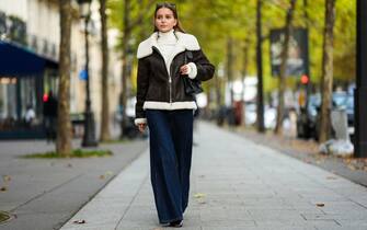 PARIS, FRANCE - OCTOBER 19: Diane Batoukina wears a brown leather aviator jacket from Massimo Dutti with white sheep wool inner lining, blue wide-leg jeans from Zara, a white turtleneck knitwear top from Massimo Dutti, black leather boots from Massimo Dutti, a Chanel bag, Chanel sunglasses, during a street style fashion photo session, on October 19, 2022 in Paris, France. (Photo by Edward Berthelot/Getty Images)