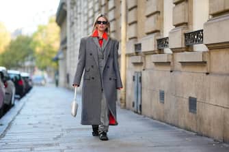 PARIS, FRANCE - OCTOBER 26: Natalia Verza wears black sunglasses, gold earrings, a neon orange shirt, a pale gray buttoned long coat, a gray oversized long coat, gray wool large suit pants, a white shiny leather Cleo handbag from Prada, black suede and white leather logo sneakers from Adidas , during a street style fashion photo session, on October 26, 2022 in Paris, France. (Photo by Edward Berthelot/Getty Images)