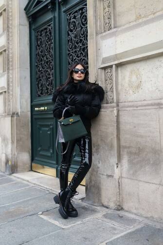 PARIS, FRANCE - DECEMBER 18: Heart Evangelista wears black sunglasses, diamonds earrings, a black nylon bomber coat with a black large fur collar, black shiny vinyl legging pants from Commando, a pale gray and dark green ostrich leather large Kelly handbag from Hermes, black shiny leather and brown LV monogram print pattern in coated canvas laces ankle boots from Louis Vuitton, black shiny leather gloves , during a street style fashion photo session, on December 18, 2022 in Paris, France. (Photo by Edward Berthelot/Getty Images)